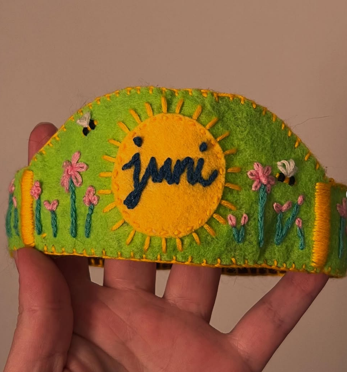 Hand holding a colorful headband with 'juuni' branding and floral design against a plain background